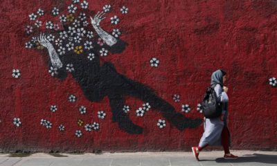 Photo of a woman walking past a mural in downtown Tehran