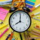 Photo of alarm clock against a backdrop of pens, rulers and paper signifying school start timesr