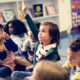 Photo of young students raising their hands in a classroom