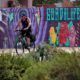 Photo of a man cycling past a mural